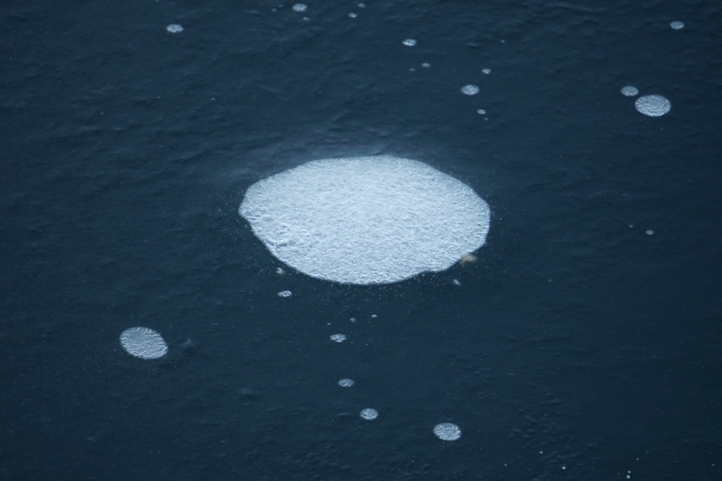 a frozen bubble under the ice is white and like a gemstone, against the ocean blue of surrounding ice